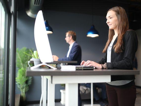 Deux personnes à un bureau réglable en hauteur, l\'une debout, l\'autre assise