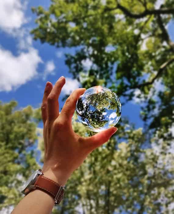 Main tenant une boule de cristal reflétant les arbres et le ciel