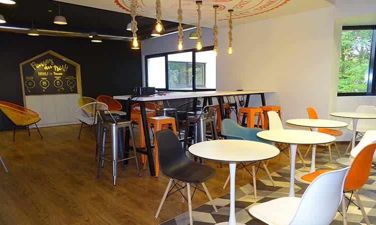 Cafétéria avec tables rondes, chaises colorées et suspensions design