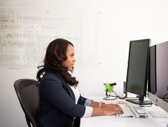 Femme travaillant à son bureau devant un écran et un tableau blanc