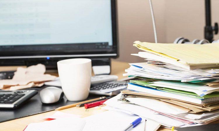 Bureau encombré de papiers et de dossiers près d\'un écran et d\'une tasse