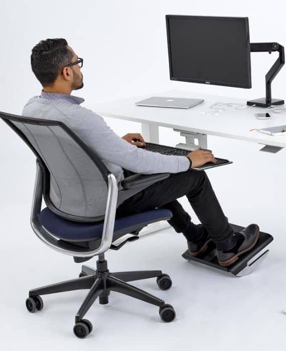 Homme assis sur un siège ergonomique avec repose-pieds à son bureau