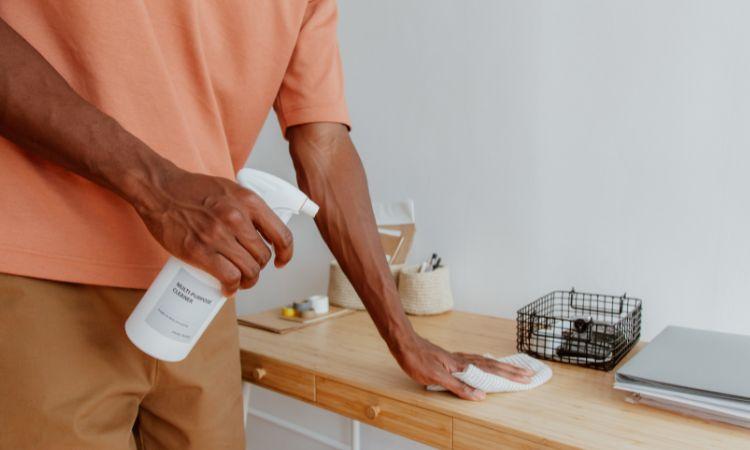 Personne nettoyant un bureau avec un spray et un chiffon