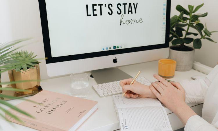 Ordinateur affichant Let\'s stay home sur un bureau avec plantes et carnet